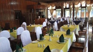 A banquet hall with tables set for dining, wooden walls, and large windows. - Nanda Wunn hotel (Nyaungshwe)
