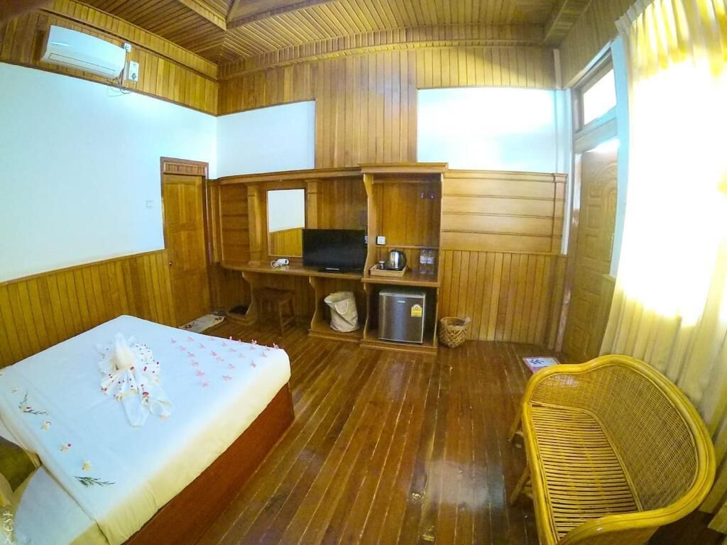 Una habitación con cama, televisión, una silla de mimbre y paneles de madera.