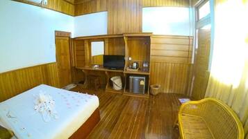 Una habitación con cama, televisión, una silla de mimbre y paneles de madera.