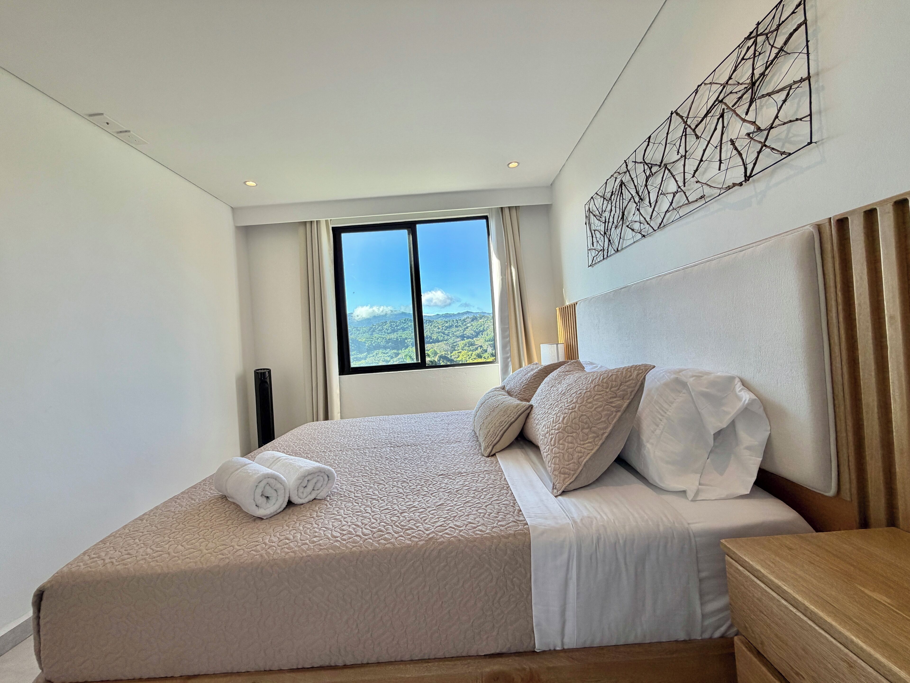 Ein Hotelzimmer mit einem großen Bett, Blick auf eine Berglandschaft, einem Kunstwerk an der Wand und einem Nachttisch mit Lampe.
