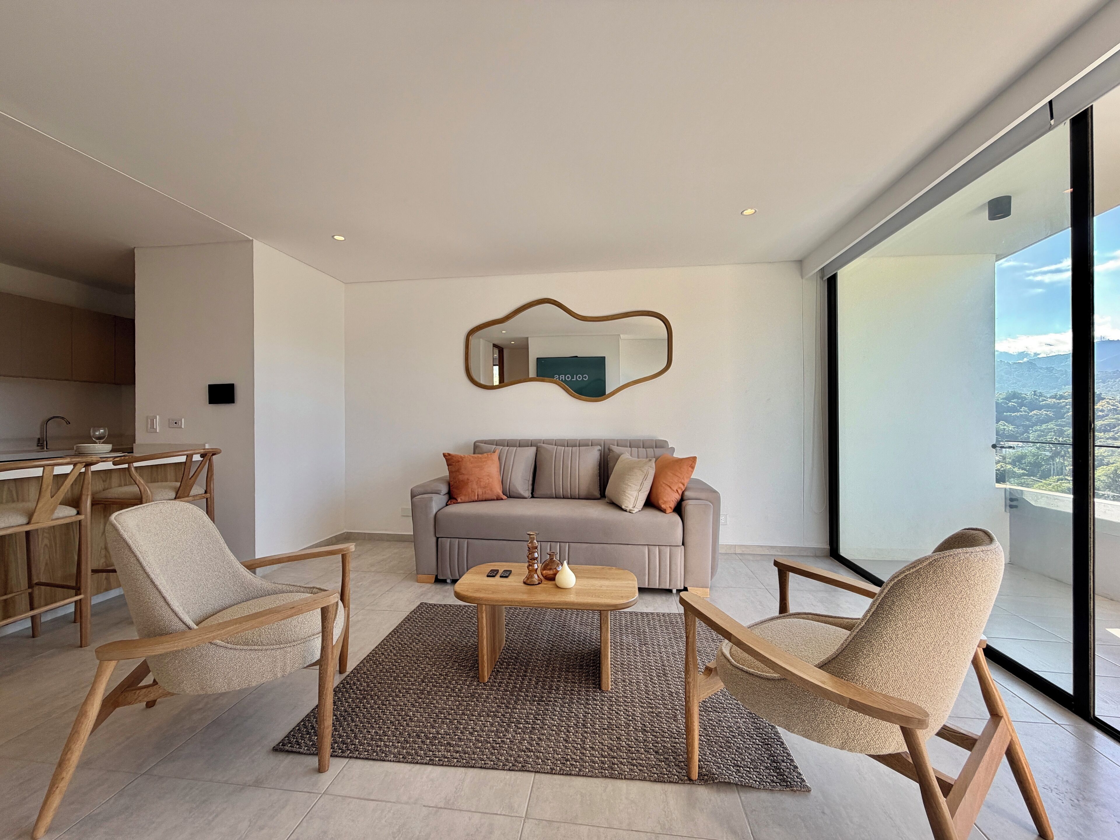 Een moderne woonkamer met een grijze bank, twee houten stoelen, een salontafel en een groot raam met uitzicht op de natuur.