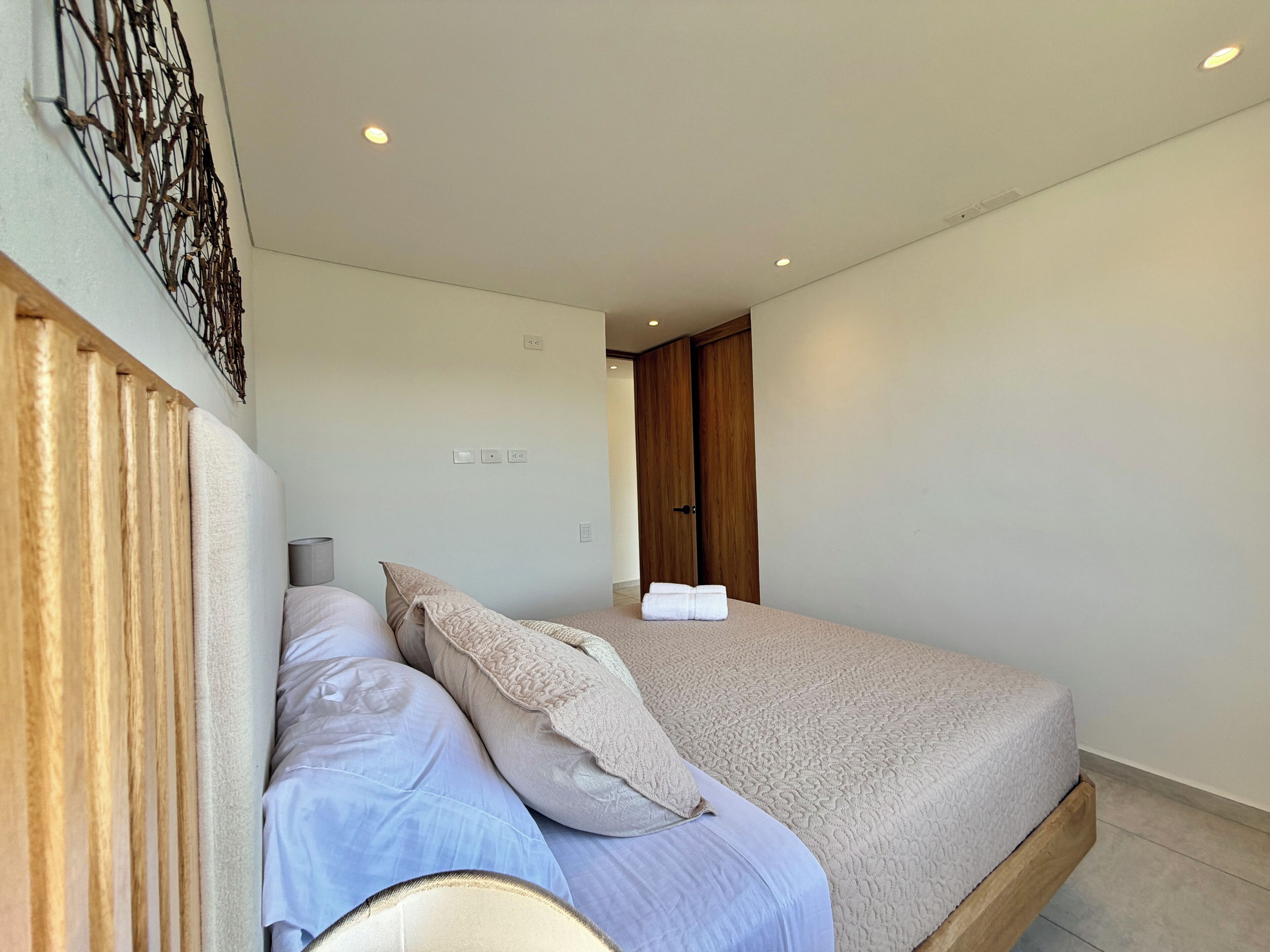 Un dormitorio con cama, almohadas y cabecera de madera. Hay dos mesitas de noche con lámparas.