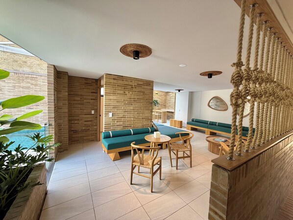 Un intérieur moderne avec un mur en briques, un canapé vert, des chaises en bois et une décoration suspendue faite de cordes.