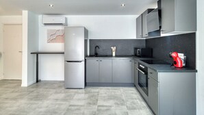 Uma cozinha moderna com armários cinza, uma geladeira de aço inoxidável, micro-ondas e um eletrodoméstico vermelho na bancada.