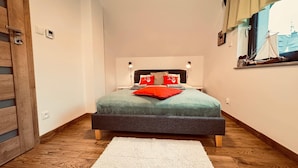 A bedroom with a bed, a nightstand, a lamp, and a window with a view of a building. - Holiday Home With Jacuzzi, for 5 People (Wladyslawowo)