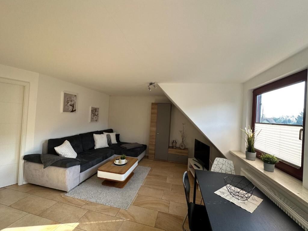 Un salon moderne avec un canapé, une table basse et une table à manger. On y trouve également un téléviseur et une cheminée. La pièce est dotée d’un plafond en pente et d’une fenêtre offrant une vue agréable.