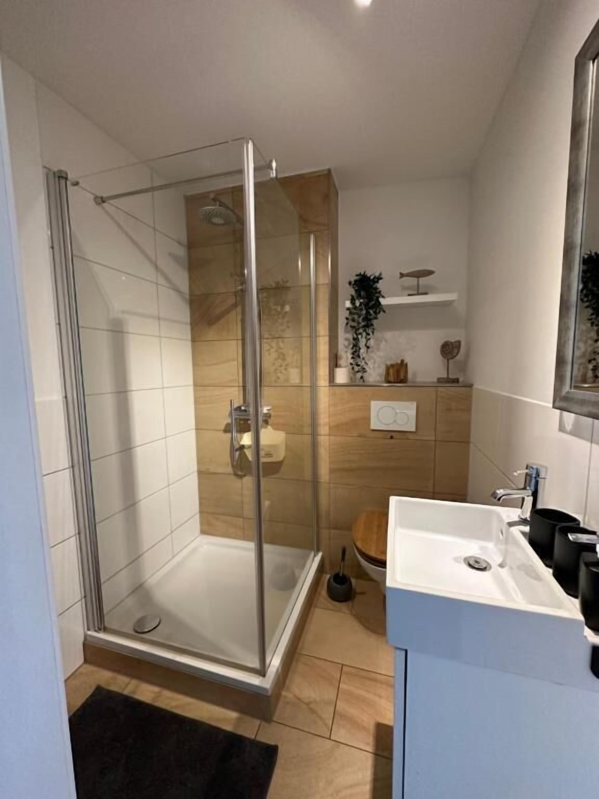 A modern bathroom with a glass-enclosed shower, a white sink, and a wooden vanity.