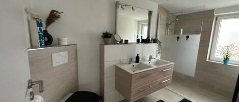 A modern bathroom with a toilet, sink, and mirror. There is a black rug on the floor and a window with a plant.