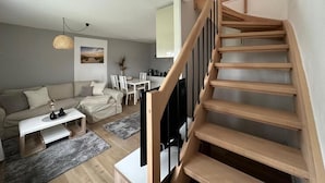 A modern living room with a wooden staircase, a sofa, a coffee table, and a dining area.