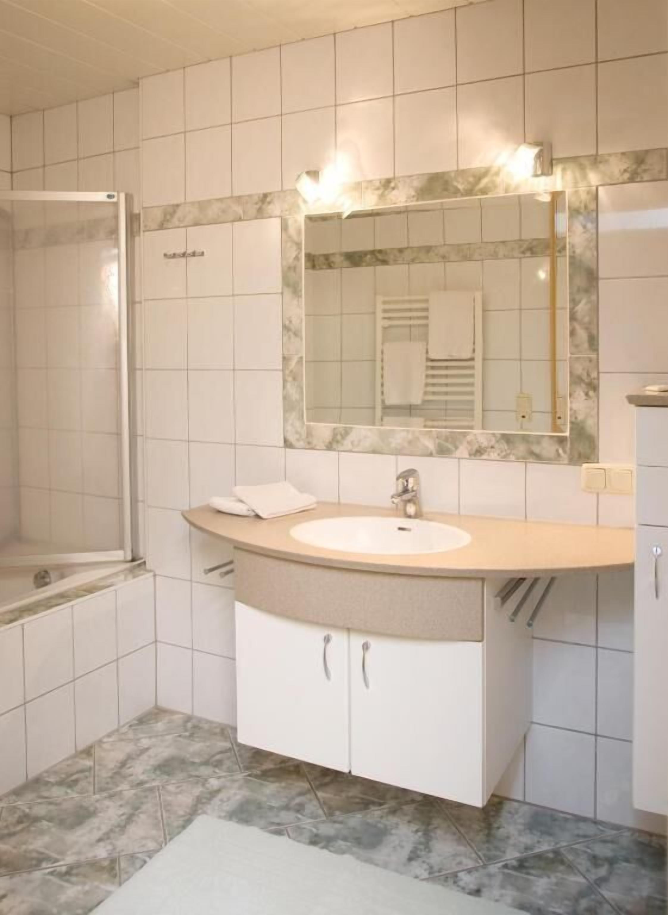 Un baño con lavamanos blanco, un espejo y una ducha.