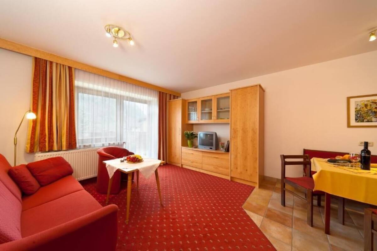 A compact room with a red sofa, a dining table with chairs, a small TV, and wooden cabinets.