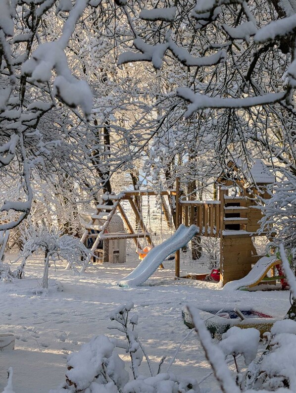 A snow-covered playground with a wooden slide and climbing structures. - The sunflower - sleeping barrel in a natural idyll with panoramic window (Holtgast)