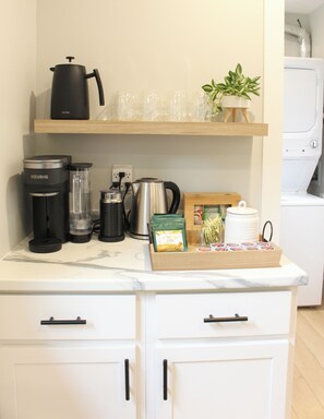 A kitchen counter with a coffee maker, a kettle, a blender, a tea box, and a potted plant. - Chelton Sanctuary | 7 Person Hot Tub, 2 King Beds, EV Charger, Full Office & A/C (Chelton)