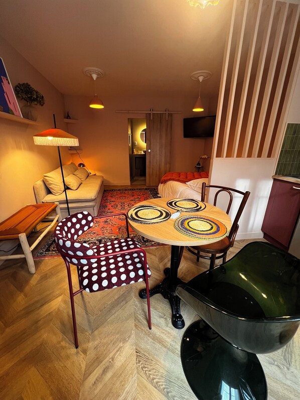 Un espace de vie compact comprenant un coin repas, un canapé, une petite table et une chaise avec un coussin à pois.