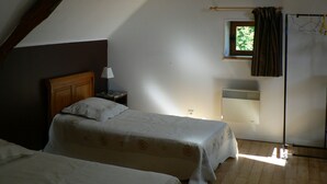 A small, dimly lit room with a sloped ceiling, a bed with a wooden headboard, a bedside table with a lamp, a small window with a view of greenery, and a radiator on the wall. - Charming gîte with large swimming pool in the Lot department (CANIAC DU CAUSSE)