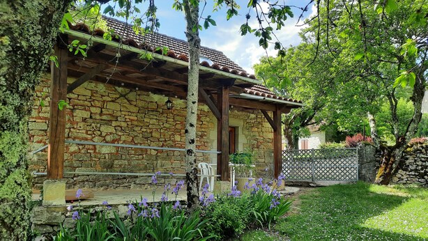 A rustic stone building with a wooden porch and a garden with purple flowers. - Charming gîte with large swimming pool in the Lot department (CANIAC DU CAUSSE)