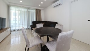 Ein modernes Wohnzimmer mit einem runden Esstisch, weißen Stühlen, einem dunklen Sofa und einem Fernseher.