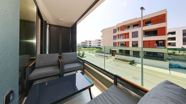 Ein Balkon mit Blick auf ein modernes Gebäude, einem Glastisch und grauen Sitzmöbeln.