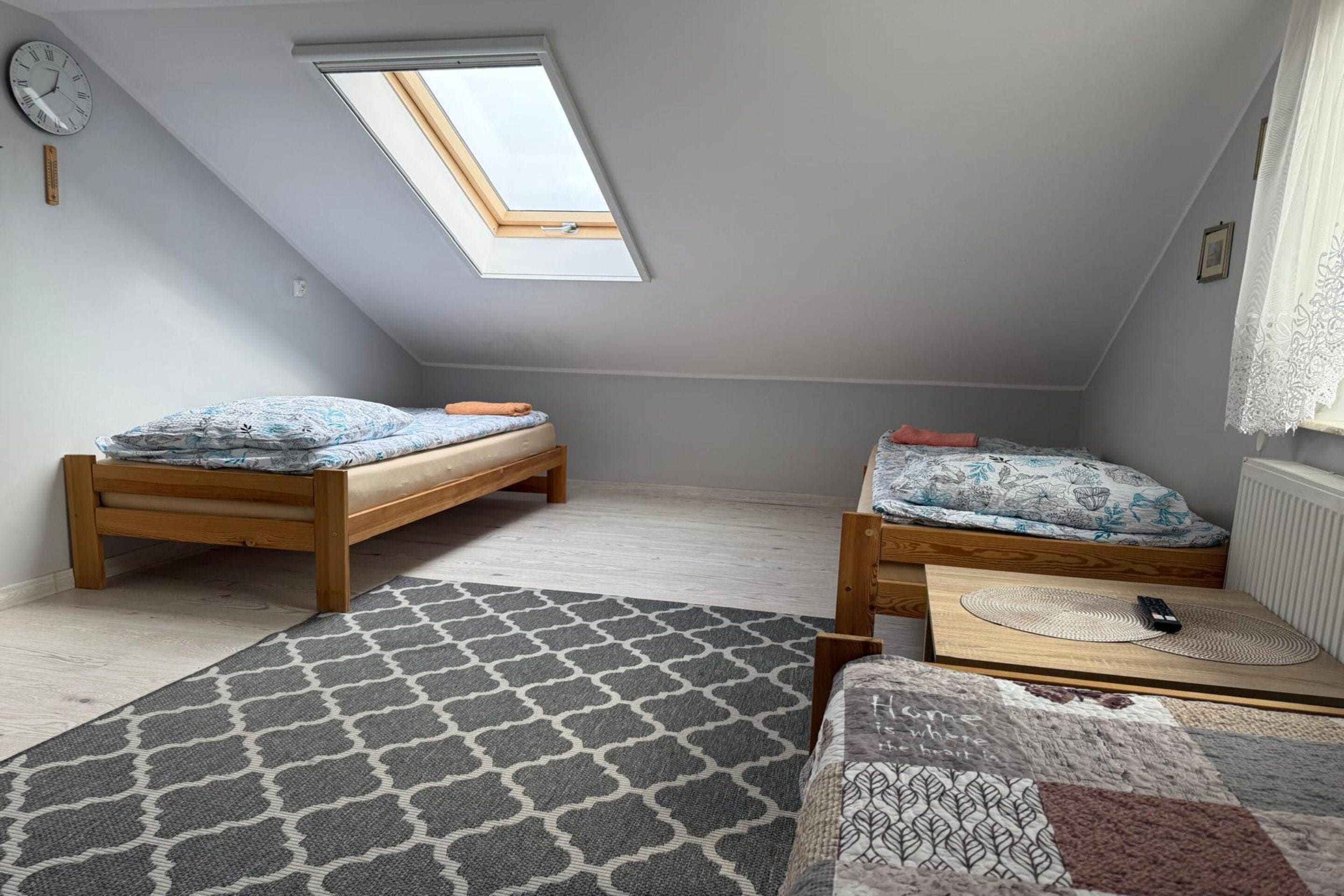 A small attic bedroom with two wooden beds, a skylight, a clock, and a patterned rug.