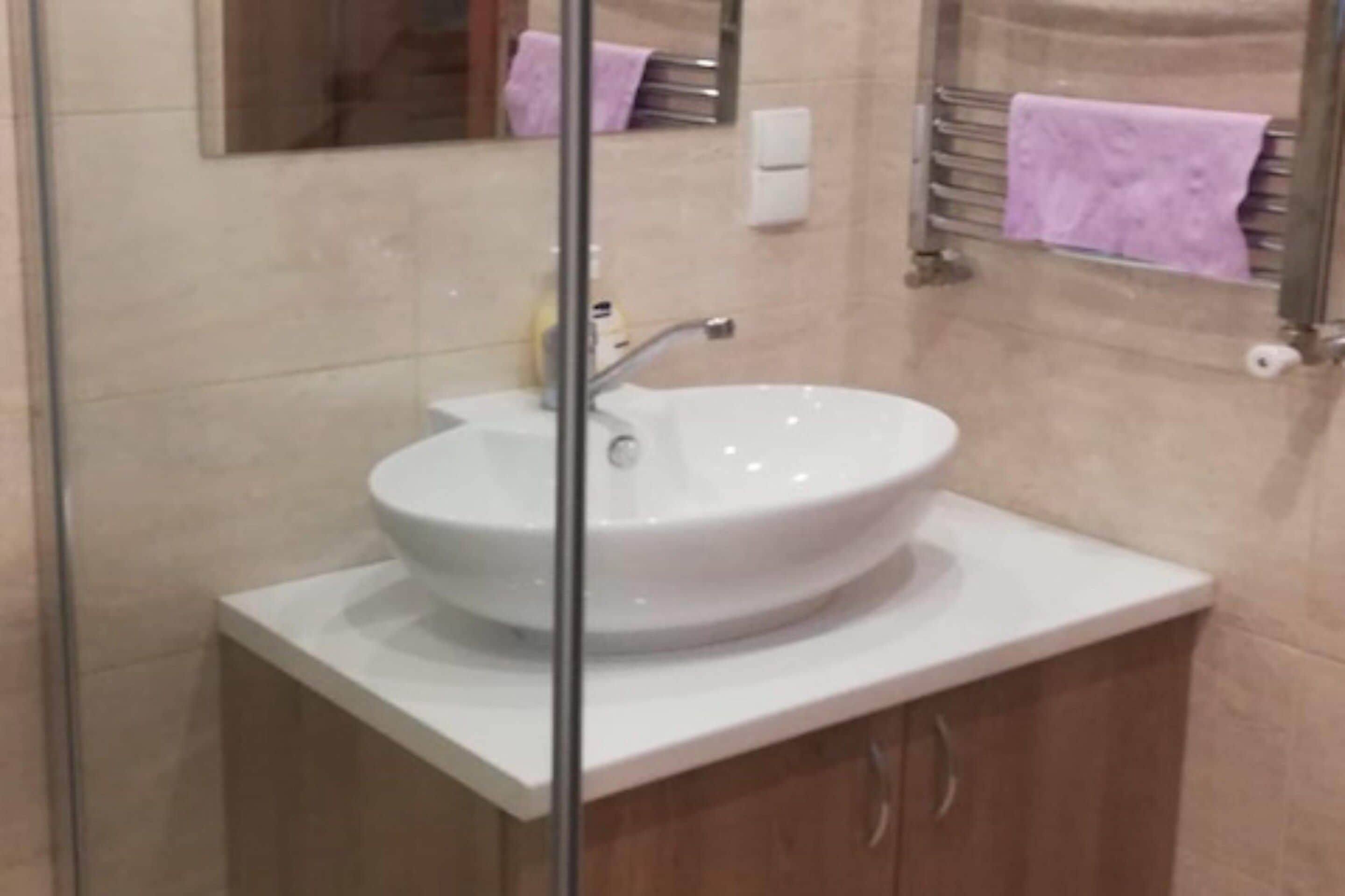 Un baño con un lavamanos blanco, un espejo y un perchero con una toalla morada.