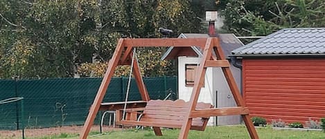 A wooden swing set in a grassy yard with a red building in the background.