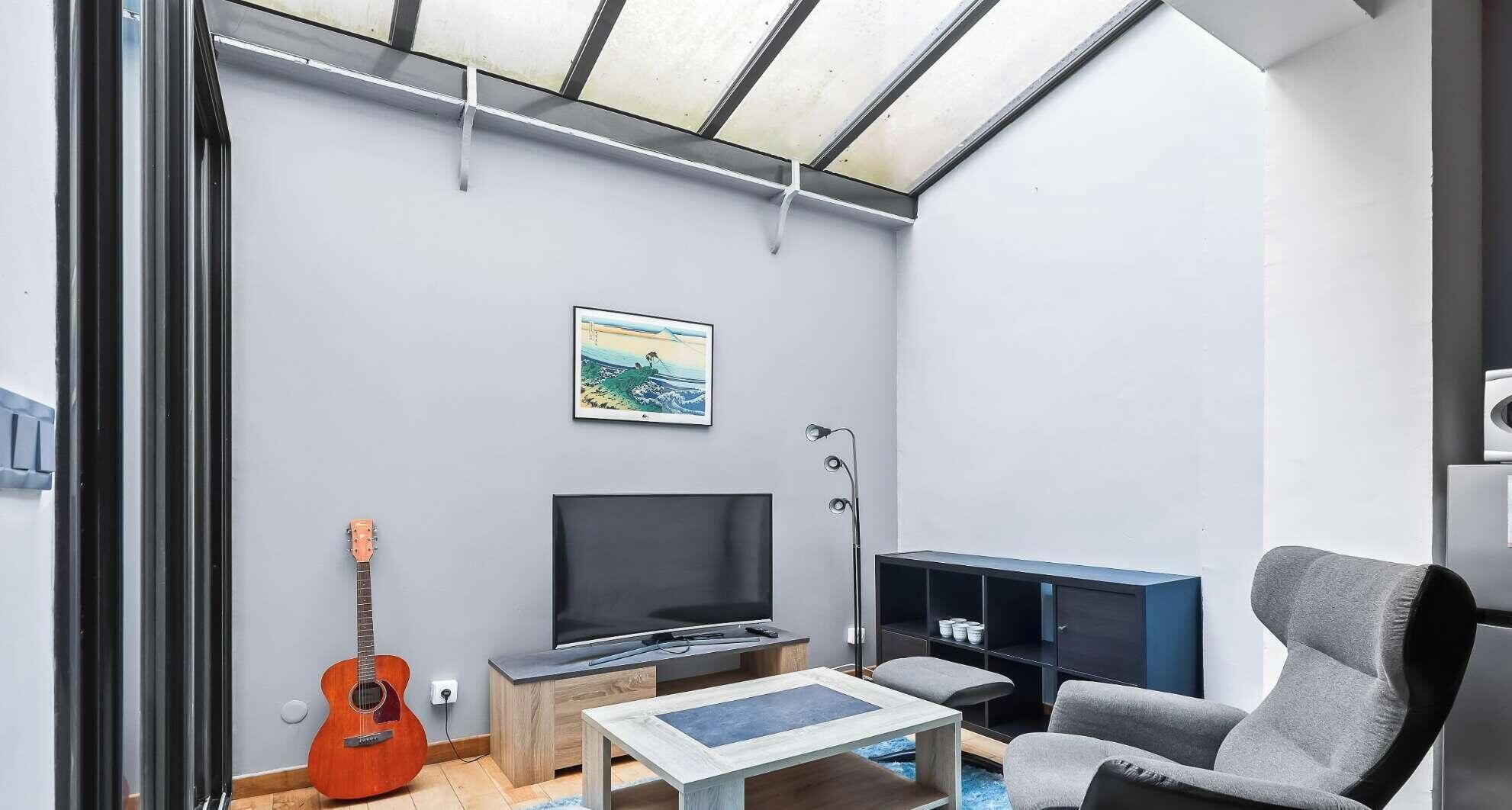 A modern living room with a flat-screen TV, a guitar, a sofa, and a coffee table.