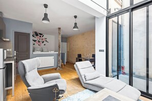 A modern living room with two grey lounge chairs, a dining area, and a kitchen. - Appartement design & confortable avec terasse (Paris)