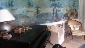 Een kamer met een grote muurschildering, een piano, een lamp en een stoel.