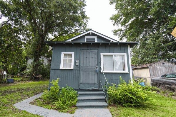 A small, single-story house with a front door, two windows, and a set of steps leading to the entrance.