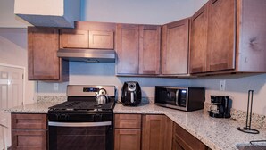 A kitchen with wooden cabinets, a stainless steel stove, a kettle, a microwave, and a coffee maker.