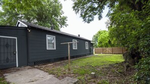 A dark-colored single-story house with a fenced backyard, a concrete patio, and a wooden fence in the background.