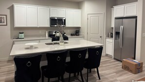 A modern kitchen with white cabinets, a stainless steel refrigerator, a microwave, and a central island with chairs. - Brand new & beautiful home in great neighborhood of N Merced (Merced)