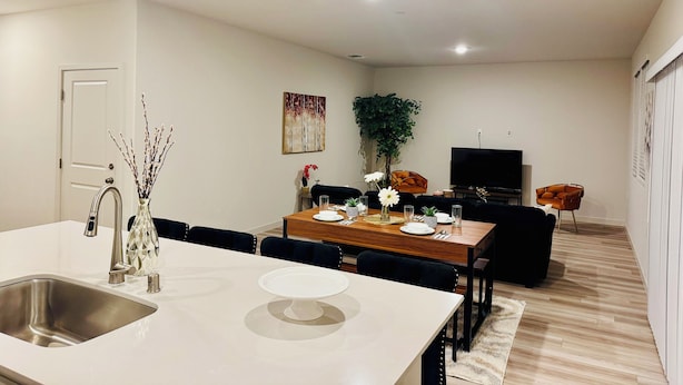 A modern kitchen with a sink, dining table, and chairs. There is a television and a plant in the living area. - Brand new & beautiful home in great neighborhood of N Merced (Merced)