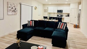 A living room with a sectional sofa, a dining table with chairs, a kitchen area with white cabinets and appliances, and a wooden floor. - Brand new & beautiful home in great neighborhood of N Merced (Merced)