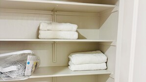 A closet with white shelves, some holding folded white towels, and a plastic bag with a label on the bottom shelf. - Brand new & beautiful home in great neighborhood of N Merced (Merced)