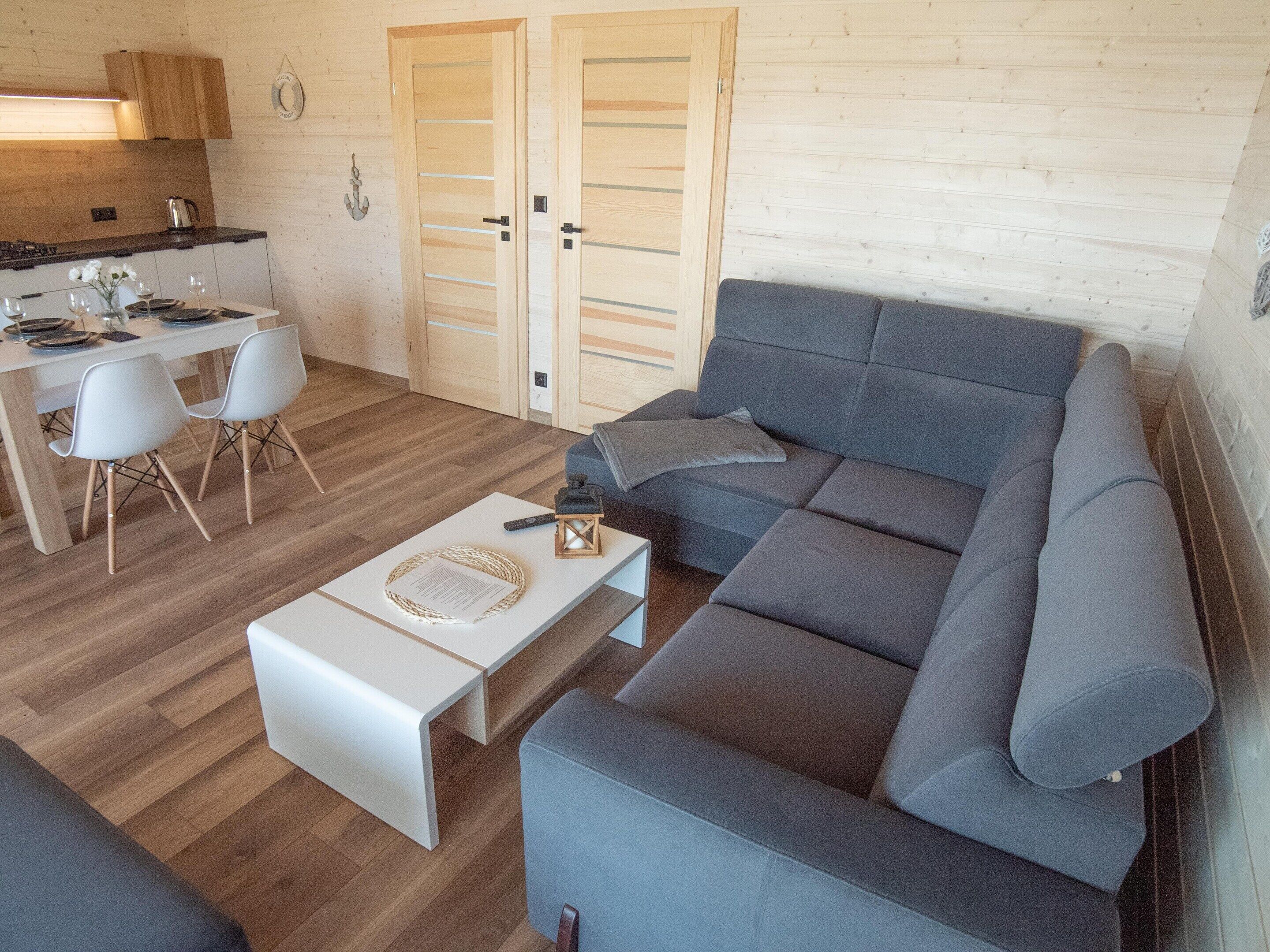 A modern living room with a grey sofa, a white coffee table, and a dining area with a wooden table and chairs.