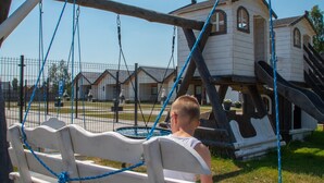 A playground with a swing set and a slide, surrounded by a fence and a building in the background. - Comfortable Holiday Homes Close to the Beach (Darlowo)