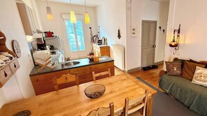 Ett mysigt vardagsrum med ett matbord i trä, en soffa och en köksdel med ett fönster.