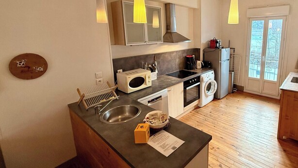 Ett modernt kök med diskho, spis, mikrovågsugn och tvättmaskin. Det finns hängande lampor och ett fönster med utsikt.