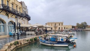 A waterfront area with boats docked, a stone wall, and buildings with balconies. - 3 Sails - 2BR on Venetian Harbour  (Chania)