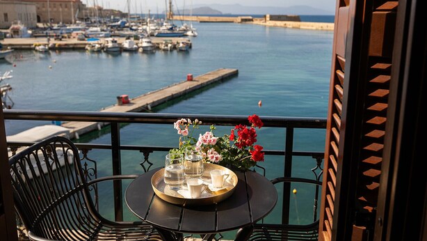A balcony with a table set for two, overlooking a marina with boats and a distant view of the sea. - 3 Sails - 2BR on Venetian Harbour  (Chania)