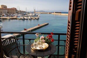 Un balcone con un tavolo apparecchiato per due, vista su una marina con barche e una lontana visuale del mare.