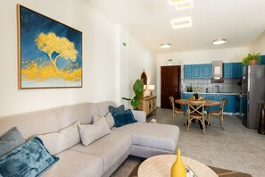 Una sala de estar con un sofá, una mesa de comedor con sillas, una cocina con armarios azules y un cuadro en la pared.