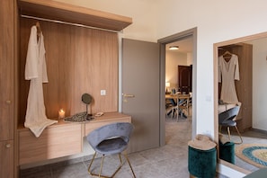 A modern bedroom with a wooden wardrobe, a vanity with a mirror, a grey chair, and a small stool.