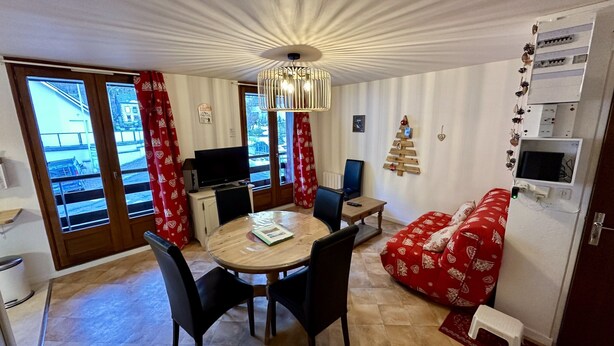 A compact living space with a dining table, chairs, a sofa, a TV, and a fireplace. - Alpine Refuge Near the Forest Road (Mont-Dore)