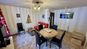 A dining area with a round wooden table, black chairs, a red patterned sofa, a wall-mounted TV, and a decorative tree on the wall. - Alpine Refuge Near the Forest Road (Mont-Dore)