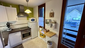A compact kitchen with white cabinets, a microwave, a stove, and a sink. There's a window with a view of a building outside. - Alpine Refuge Near the Forest Road (Mont-Dore)