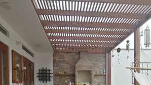 Ruim terras met een houten pergola, een eettafel met stoelen en een keukengedeelte met een stenen achterwand.
