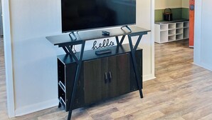 Ein Wohnzimmer mit einem Flachbildfernseher auf einem schwarzen TV-Schrank, einer Wanduhr und einem Schild mit der Aufschrift 'hello'.