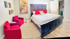 Ein Schlafzimmer mit einem großen Bett, einem roten Sessel, einer Holzkommode und einem Gemälde an der Wand.